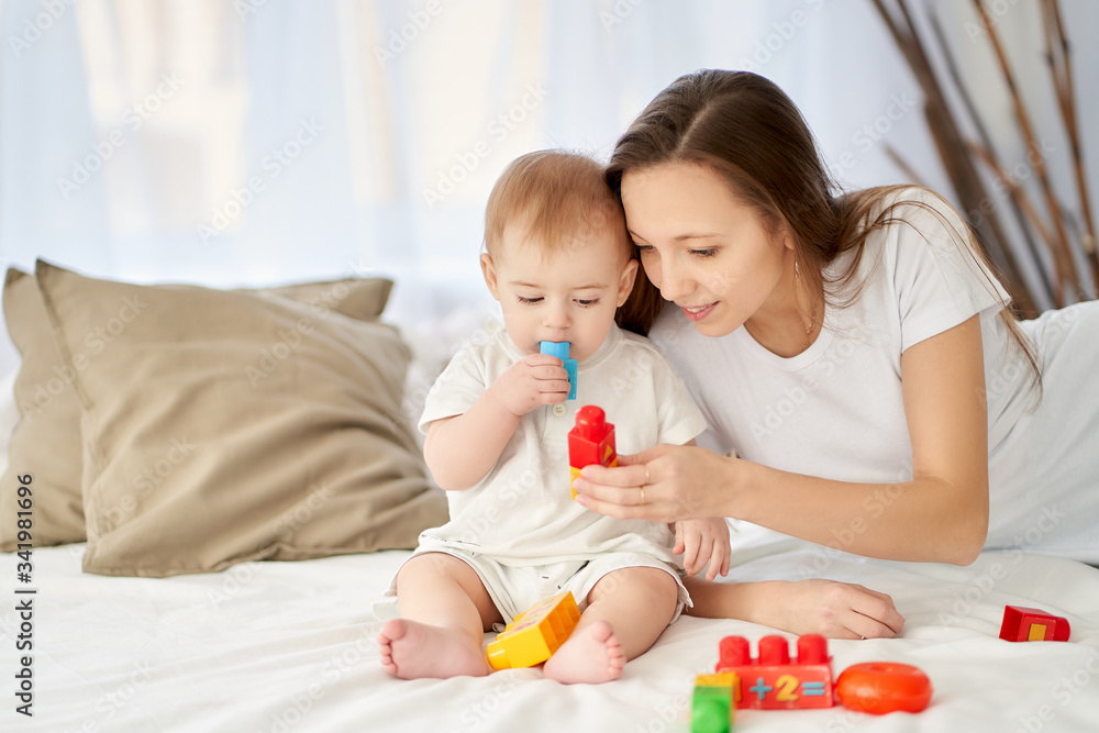 In a bright room on the bed, mom plays cubes with the baby, he tastes them. In a bright room on the bed, mom plays cubes with the baby, he tastes them.