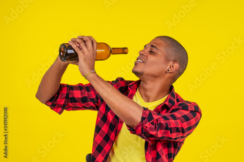 latin brazilian man holding alcohol bottle in studio yellow background
