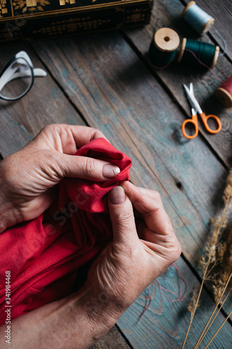 Female hands sewing on wooden table, scissors, casket, thread, glasses