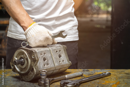 Professional mechanic man inspection hydraulic gear pump of wheel loader in workshop, repair maintenance heavy machinery photo