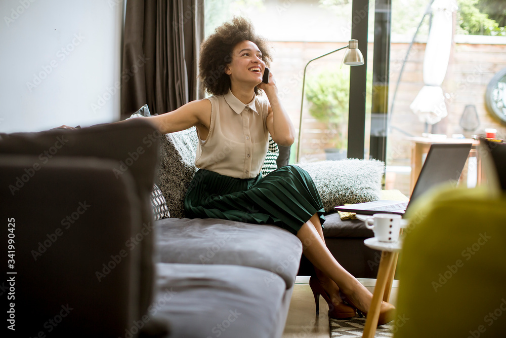 Young curly hair african woman relaxing at home and using mobile phone