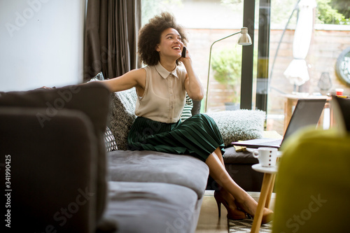 Young curly hair african woman relaxing at home and using mobile phone