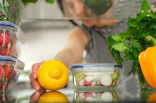 Woman looking inside a fridge full of food and choosing a lemon.