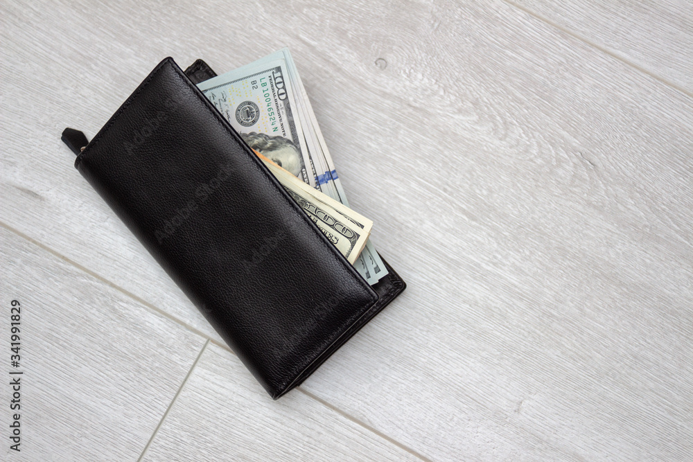 Black leather wallet with american dollars on a background of gray wood floor, close-up. Full of money. Wealth and prosperity concept Black leather wallet with american dollars on a background of gray wood floor, close-up. Full of money. Wealth and prosperity concept
