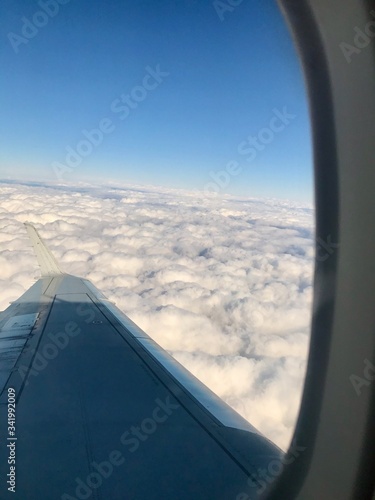 Beautiful view out of the airplane window inside the cabin of a business flight  The aircaft s wing is floating through an unreal heaven of spectacular fluffy white clouds in the atmosphere