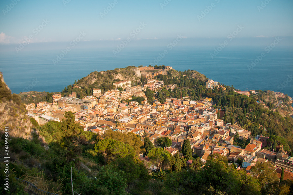 Beautiful panorama from mountain top to a small mediterranean sicilian town, Taormina, in warm sunset with the sea in the background, Sicily, Italy	
