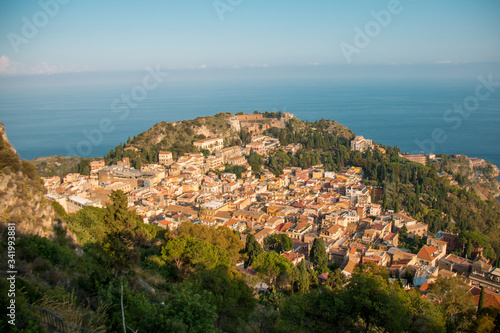 Beautiful panorama from mountain top to a small mediterranean sicilian town, Taormina, in warm sunset with the sea in the background, Sicily, Italy 