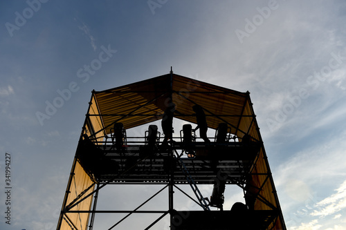 Technical staff and equipment silhouetted against sunset light preparing for a music concert