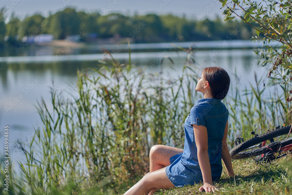 Weekend, outdoor recreation. The girl, leaning on her hands, sits by the lake with reeds. Side view. Weekend, outdoor recreation. The girl, leaning on her hands, sits by the lake with reeds. Side view.