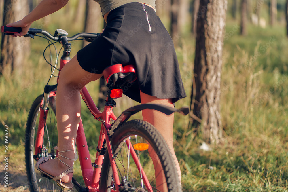 teen girl on a red bicycle seat close-up, rear view. female foot in sandals on a background of grass and trees. teen girl on a red bicycle seat close-up, rear view. female foot in sandals on a background of grass and trees.