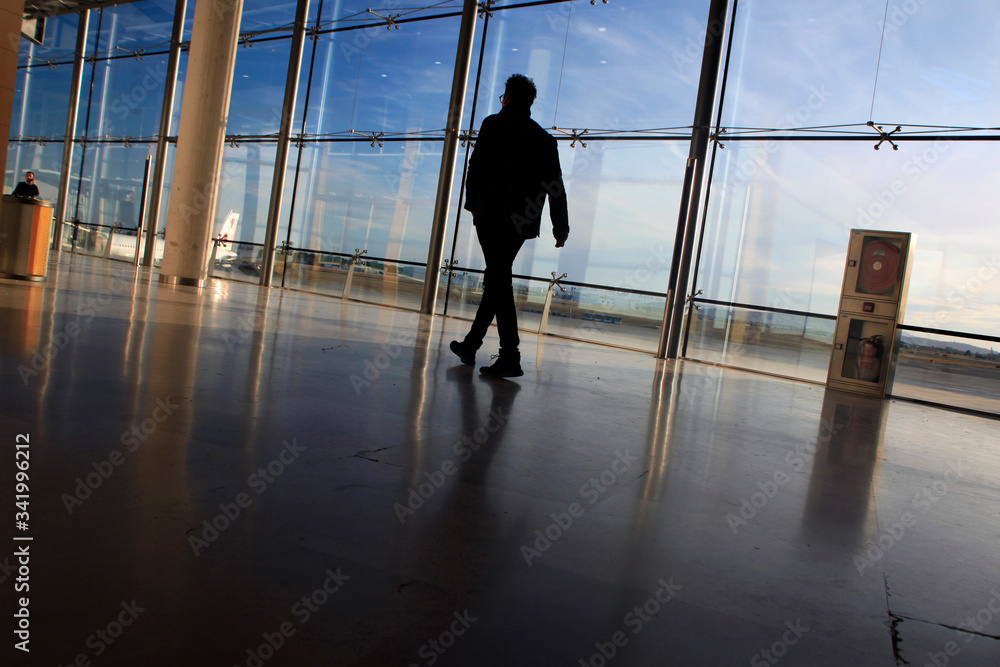 A man walking in the airport backlit with a large window behind A man walking in the airport backlit with a large window behind