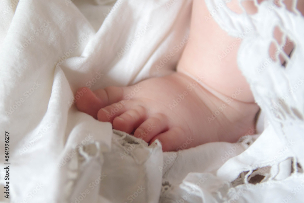 Leg of a child, a newborn in a white diaper with embroidery. The tender baby is lovingly wrapped in a blanket. Leg of a child, a newborn in a white diaper with embroidery. The tender baby is lovingly wrapped in a blanket.