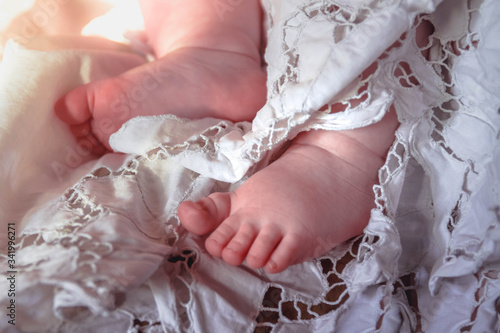 Leg of a child, a newborn in a white diaper with embroidery. The tender baby is lovingly wrapped in a blanket.