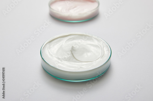 Selective focus of laboratory glassware with white and pink cosmetic cream on grey background