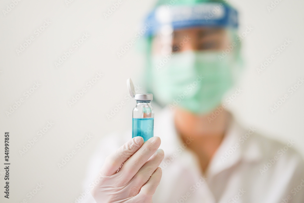 Selective focus of bottle with Coronavirus vaccine for 2019-nCoV COVID virus and blur medical doctor wearing PPE suit Selective focus of bottle with Coronavirus vaccine for 2019-nCoV COVID virus and blur medical doctor wearing PPE suit