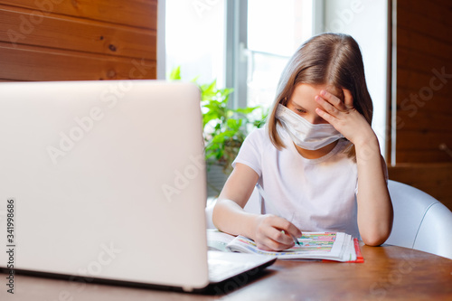 Home schooling. A girl is sitting at a table with a laptop during an online video chat of a school lesson with a teacher and class. Concept of distance education. Self-isolation in quarantine