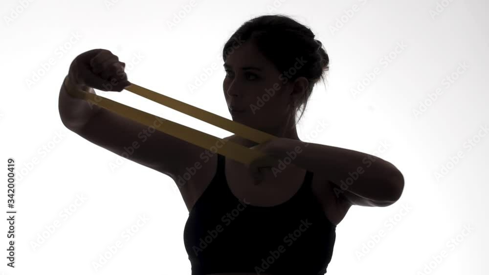 silhouette figure of young athletic woman exercising arm muscles with elastic rubber band on a white isolated background, fit girl exercising, concept female beauty and healthy lifestyle silhouette figure of young athletic woman exercising arm muscles with elastic rubber band on a white isolated background, fit girl exercising, concept female beauty and healthy lifestyle