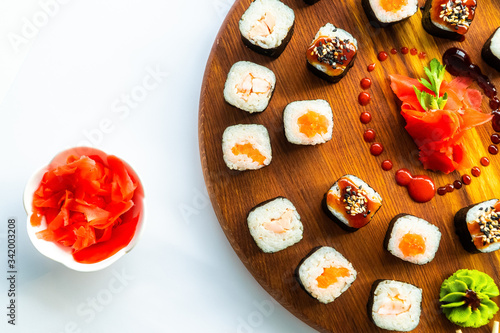 Different sushi on a round wooden surface with ginger on white background