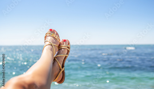 Photography Beautiful female legs in sandals against the background of the sea on a sunny day