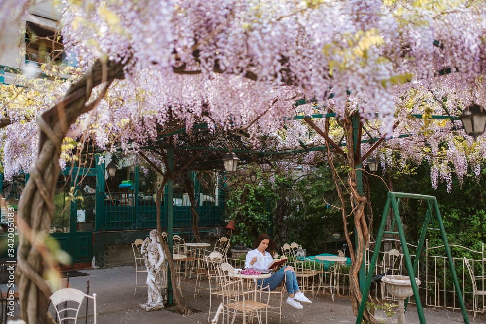 Obraz premium A beautiful young caucasian girl is reading a book in the garden. Spring and flowers