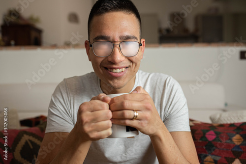 Принти на полотні portrait of young man at home holding a cup of tea  and smiling with spectacles fogged lenses