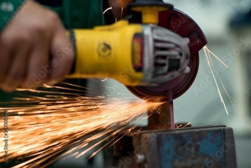 Worker cutting metal hand work angle grinder sparks.