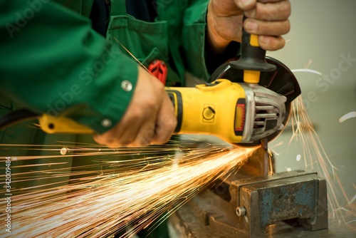 Worker cutting metal hand work angle grinder sparks.