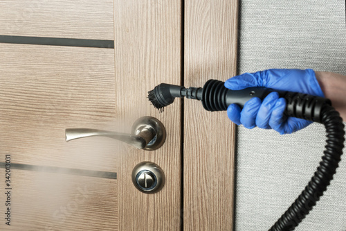 cleaning  door handle with steam generator, hand in blue glove holds steam genetator and hose with brush, which produces steam for disinfection from microbes, dirt and viruses, home cleaning concept