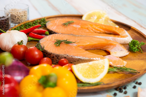 Fresh raw salmon steak with colorful vegetable and hot spice ingredient on wood plate in color wood plank background