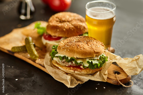Homemade beef burgers with a glass of beer, tomatoes, cheese, sauce on wooden cutting board