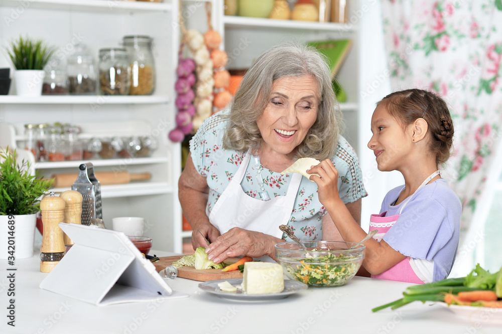 Cute little girl with her grandmother cooking together at kitchen table