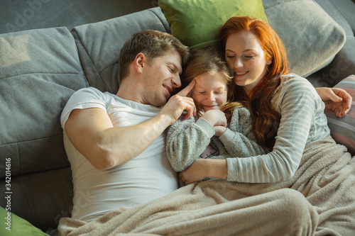Lovely. Family spending nice time together at home, looks happy and cheerful. Mom, dad and daughter having fun, lying down the sofa. Togetherness, home comfort, love, relations concept.
