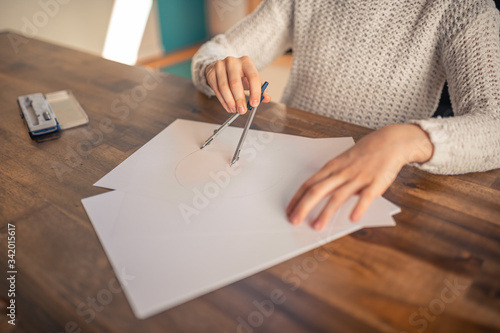 Beautiful 9 year old brunette girl drawing with compasses with shiny bright background studying geometry