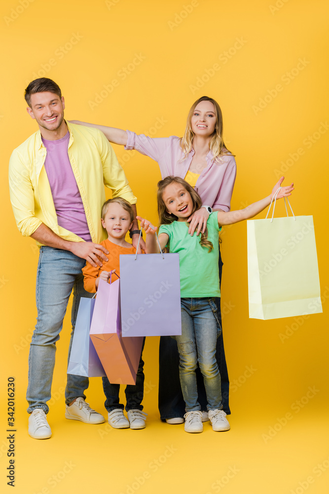 cheerful parents and excited kids with shopping bags on yellow