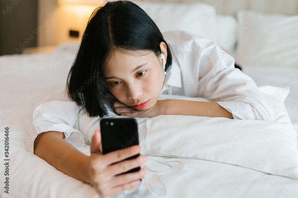 Beautiful asian female in white shirt calling mobile phone while working on bed. work from home concept. Beautiful asian female in white shirt calling mobile phone while working on bed. work from home concept.