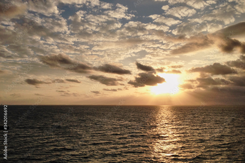 Breathtaking sunset in the middle of the ocean, with yellow orange blue sky and white clouds, View from the deck of cruise ship. Travel vacation voyage landscape.