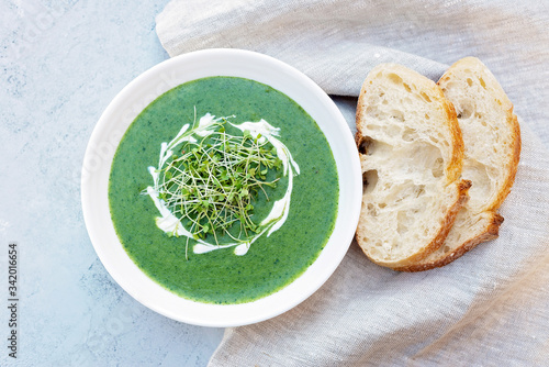 Cream soup of fresh spinach with cream and arugula microgreen in a white plate with ciabatta bread on a light gray background. Healthy and diet food. Flat lay.