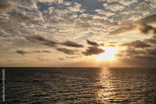 Breathtaking sunset in the middle of the ocean, with yellow orange blue sky and white clouds, View from the deck of cruise ship. Travel vacation voyage landscape.