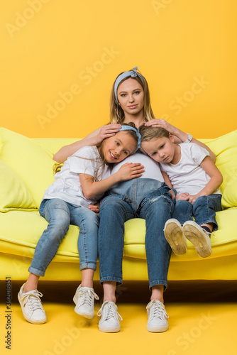 smiling pregnant mother hugging with happy daughter and son on sofa on yellow