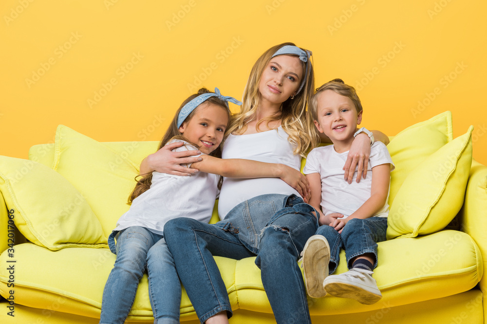 happy pregnant mother hugging with kids on sofa isolated on yellow happy pregnant mother hugging with kids on sofa isolated on yellow