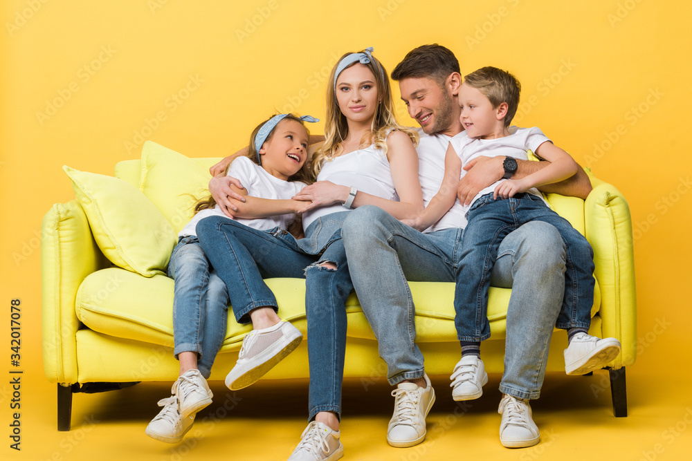 smiling pregnant mother, father and kids sitting on sofa on yellow