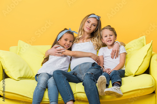 happy pregnant mother hugging with kids on sofa isolated on yellow © LIGHTFIELD STUDIOS