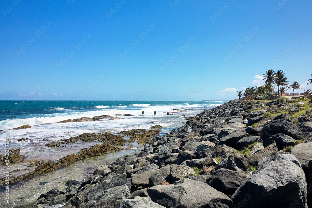Coastline with huge stones. Ocean view with rocky beach.Tropical island landscape with turquoise sea, foamy waves and palm trees. Travel vacation.