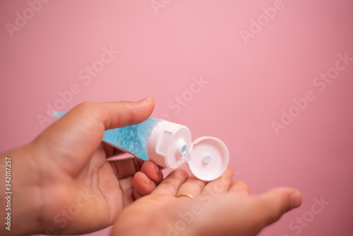 Close up hand holding alcohol gel bottle on pink pastel background.