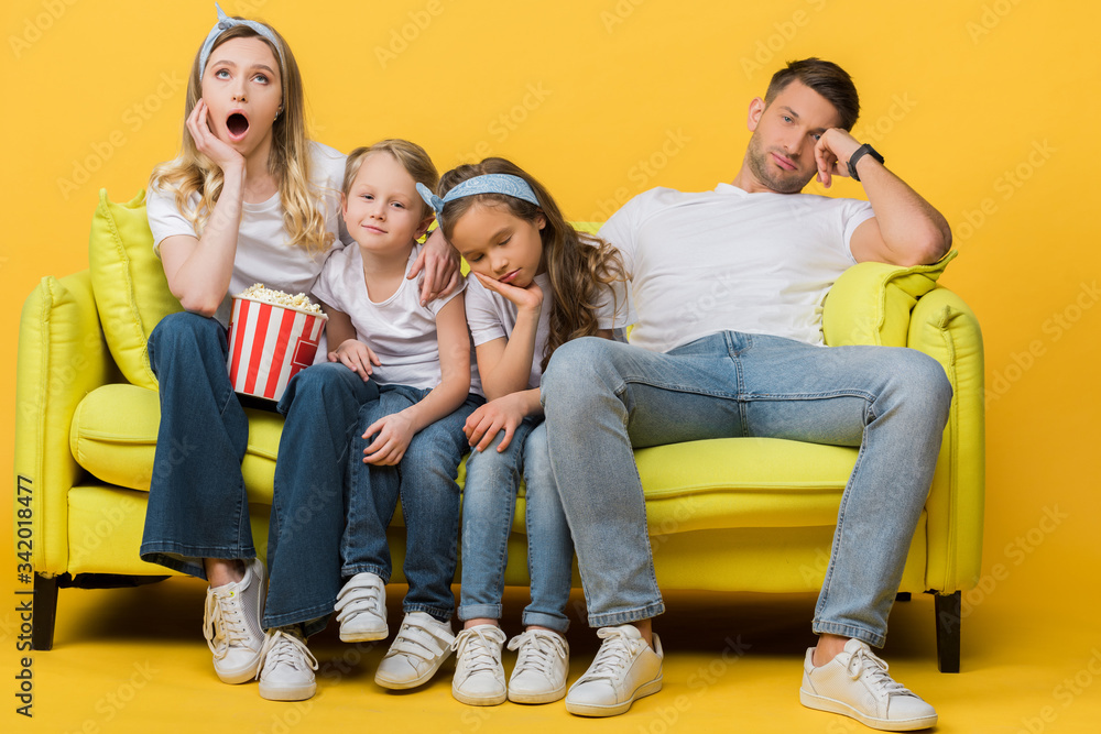 bored parents and kids watching movie on sofa with popcorn bucket on yellow bored parents and kids watching movie on sofa with popcorn bucket on yellow
