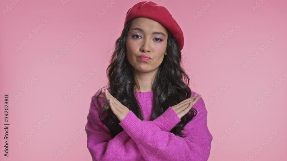 Serious young asian woman posing isolated over pink wall background say no make stop gesture. Serious young asian woman posing isolated over pink wall background say no make stop gesture.