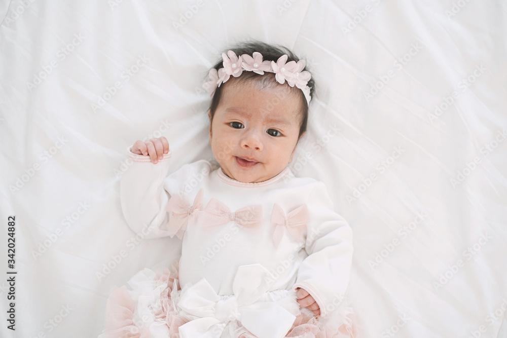 Adorable little baby girl in a beautiful dress with flower band lying on a white blanket. Adorable little baby girl in a beautiful dress with flower band lying on a white blanket.