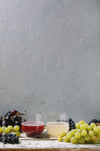 Traditional New european low alcohol red and white wine Federweisser or Neuer Wein, Burcak, Vin bourru in glasses with black and green grapes bunches on old white wooden table. Copy space. photo