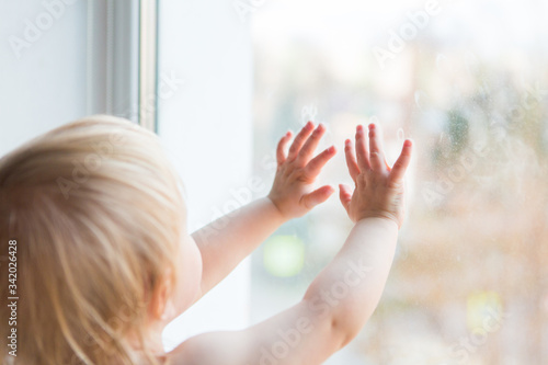 Little girl looking at window. One year child touching the glass