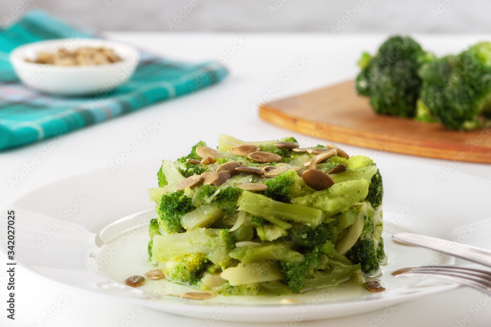 Boiled broccoli with pumpkin seeds on a white plate on the table